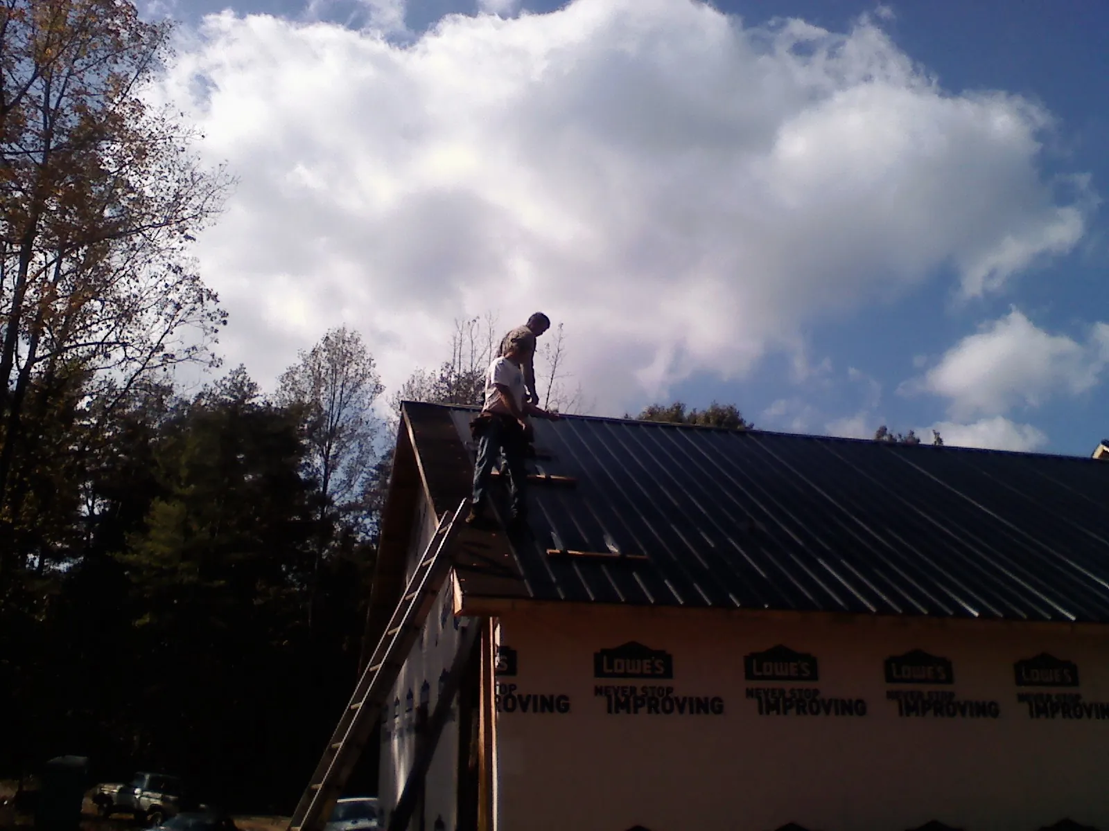 Roofer fastening dark metal panels high against a cloudy sky, from a Roof Inspection job in Winslow